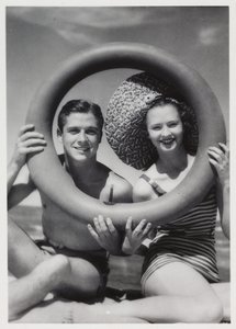 Man and woman looking through a rubber ring on beach, c 1935