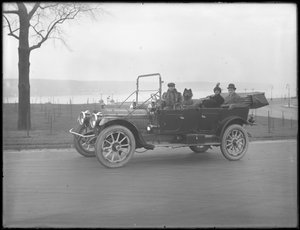 Three unidentified people and two Chow dogs driving in a convertible car along a river or lake by William Davis Hassler