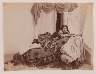 Studio shot of a reclining lady reading a book by Antoin Sevruguin