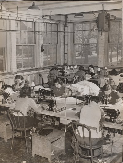 Women Seated at Desks Work on Sewing Machines by Arnold Eagle