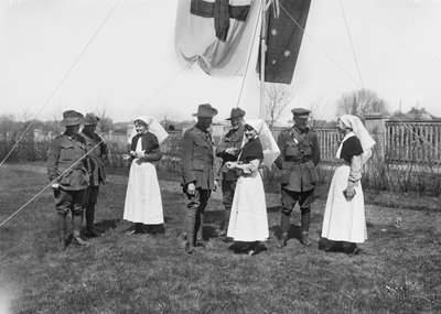 A group of unidentified officers, nurses and men of the 3rd Australian Casualty Clearing Station gathered beneath a flag pole flying the Australian flag and the Red Cross flag by Australian Photographer