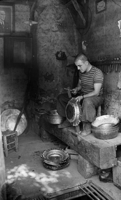 Italian metalworker hammering on a form sheet metal to make a raised vessel or pot, Italy by Bernard F. Rogers