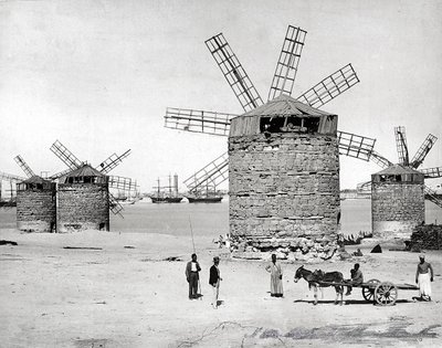 Windmills on the Mediterranean Sea in Alexandria, Egypt. In front, some Egyptians posing with a small cart by Brothers Zangaki