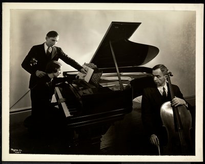 Blind woman, Miss Harding, at the piano instructing two blind men on the violin and cello, 1936 by Byron Company