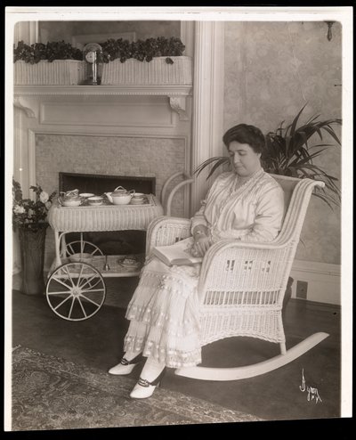 Mrs. Howard Seated with a Book in a Rocking Chair at Her Home at 200, 5th Avenue, New York, 1915-6 by Byron Company