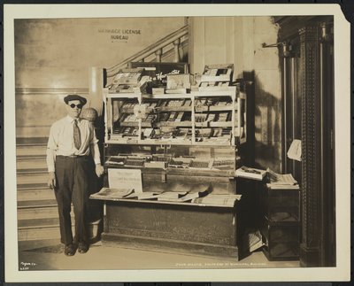 Blind news dealer, John Martie, at his stand at the south end of the Municipal Building, New York by Company Byron