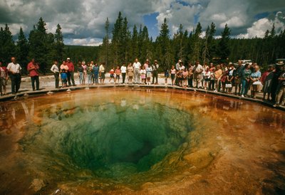 Park visitors gather around blue-green, blossom-shaped thermal pool. Yellowstone National Park by Dean Conger