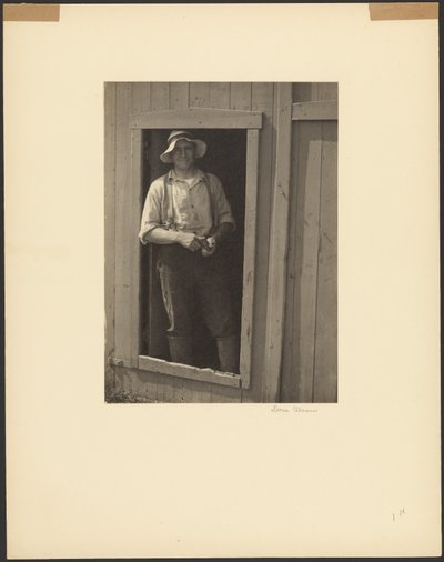 Man in a Straw Hat Standing in Doorway of a Barn Holding a Tobacco Pouch by Doris Ulmann