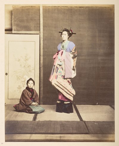 Full-length standing studio portrait of a young woman in elevated shoes, her young attendant kneeling on the floor beside her by English Photographer