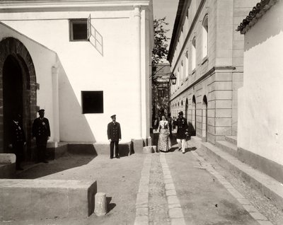 Men in uniform accompanying an elegantly dressed woman towards the church of the farm of Lo Zucco, Sicily by Eugenio Interguglielmi