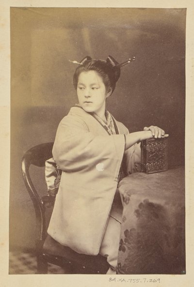 Seated Japanese woman holding a cartes-de-visite album at a table by Felice Beato