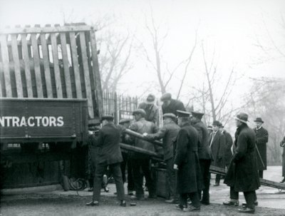 A crowd of onlookers stand by as a Rhinoceros is unloaded from a truck, by keepers, at London Zoo in 1924 by Frederick William Bond