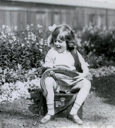 A young girl Betty holding an Eastern Indigo Snake, while sitting on a leather trunk, London Zoo, 1924 by Frederick William Bond