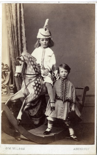 Young girl with hat on rocking horse with another girl standing by by George Washington Wilson