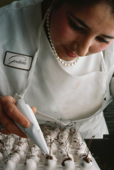 A Godiva chef attaches chocolate stems to fondant-covered cherries, Brussels, Belgium by James L Stanfield