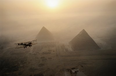 The vintage airplane Vimy flies above fog-shrouded pyramids during a golden sunrise by James L Stanfield