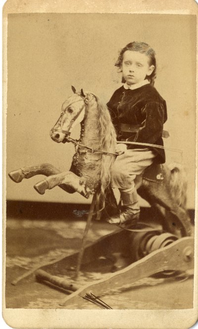 Young boy with whip on rocking horse by John McCaffrey