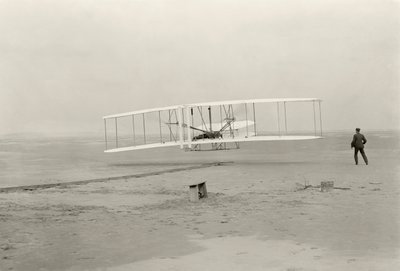 The Wright Flyer I makes its first flight of 120 feet in 12 seconds, at Kitty Hawk, North Carolina by John T. Daniels