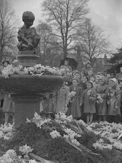 Children placing bunches of daffodils on fountain with statue on top by Joseph Hardman