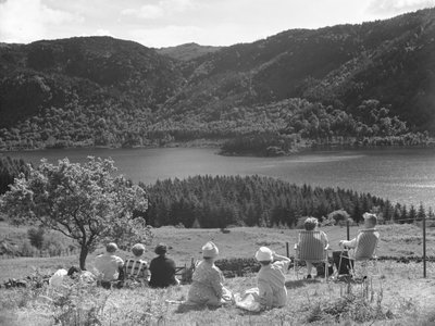 Group of people sitting on grass or deck chairs looking at a view of Thirlmere by Joseph Hardman