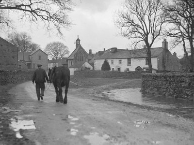 Man leading horse down road toward village buildings and church by Joseph Hardman