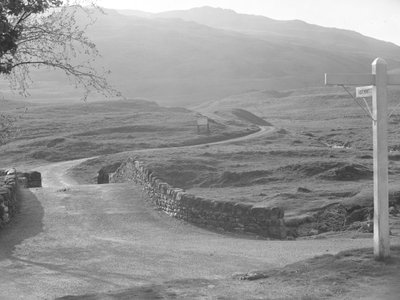 View of the road passing over Hardknott Pass with a sign pointing in the direction of Hardknott by Joseph Hardman