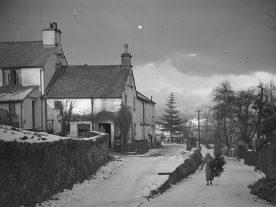 Woman carrying branch on road next to Borwick Fold Farm in Hawkshead in snow by Joseph Hardman