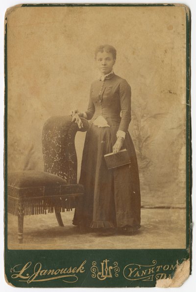 Photograph of a woman standing next to a chair and holding a book by Louis Janousek