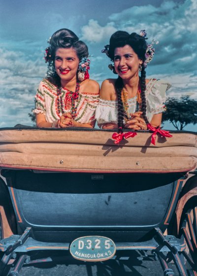 Young Nicaraguan women pose in festive costumes and headgear in back of a carriage by Luis Marden