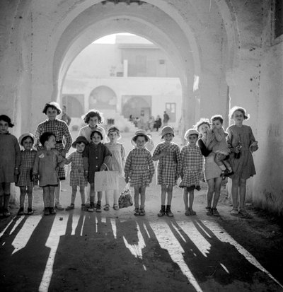 European children in school uniform under arch with shadows by Maynard Owen Williams