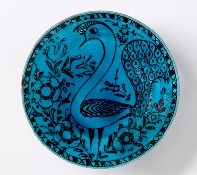 A 19th century Persian pottery dish depicting a peacock on a turquoise background by Persian School