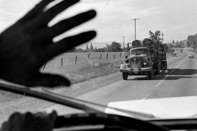 Driver in logging truck waves to another logging truck by Ted Spiegel