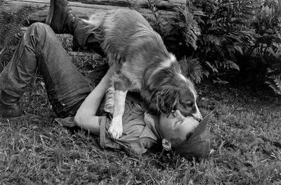 Young Man Plays with His Dog Outside Their Log Cabin in Palmer, Alaska by Ted Spiegel