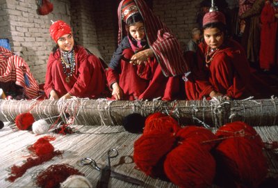 Turkoman tribeswomen weavers trim knots in the warp of a rug on a loom in a village by Thomas J. Abercrombie