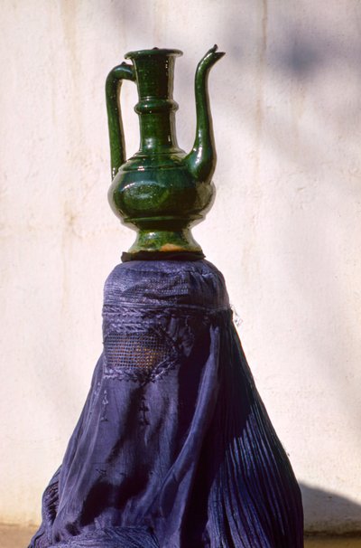 Woman in Kabul secluded from view by silk chadri carries jug by Thomas J. Abercrombie