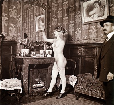 Enigmatic photograph showing a young woman completely naked (except for her shoes and stockings) recoiffing her hair in front of a mirror in the presence of a man dressed and heated with a hat. One might think it was a photo taken in a brothel, but this hy by Unbekannter Künstler