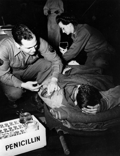 Second World War: Luxembourg February 1945: In a US Army evacuation hospital, a medic (nurse) administers penicillin to an injured soldier to avoid infection while a nurse prepares him for an operation by Unbekannt