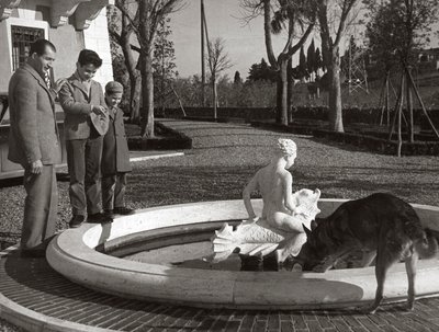 Gino Bartali with two kids and a dog near a fountain by Unknown photographer