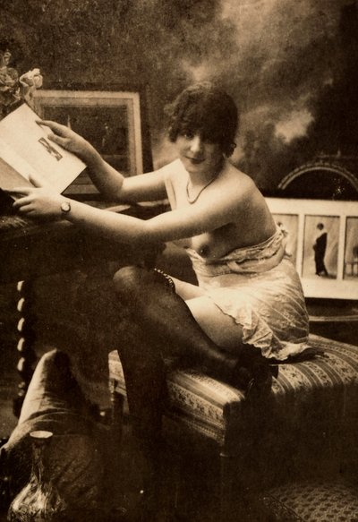Portrait of a young woman in intimate apparel, seated at a table with a book by Unknown photographer