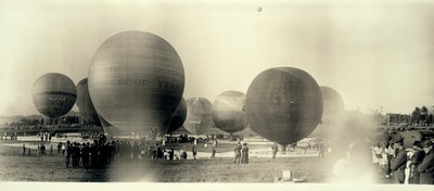 Hot air balloons at a field in South St. Louis ready for launch; one is already in the sky in the distance by W.C. Persons