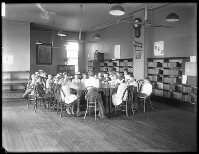 Children listen to a woman in the reading room of an unidentified branch of the Queens Borough Public Library, c.1910 by William Davis Hassler