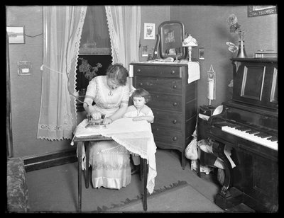 Unidentified woman demonstrating the use of an electric iron, watched by little girl, c.1913-14 by William Davis Hassler
