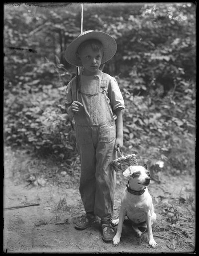 William Gray Hassler in straw hat and overalls, carrying fishing pole and basket, posed in the woods with a small dog (Bessie) by William Davis Hassler