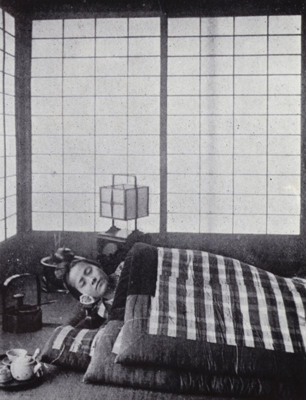 Girl asleep between wadded quilts with a wooden pillow by American Photographer (after)