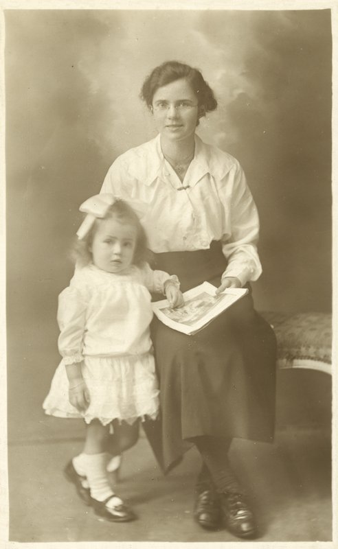 Pretty girl, mother or governess, showing photos to young child by English Photographer