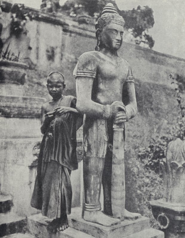 Young Buddhist novice monk beside a statue of the Buddha, French Indochina by Ewing Galloway
