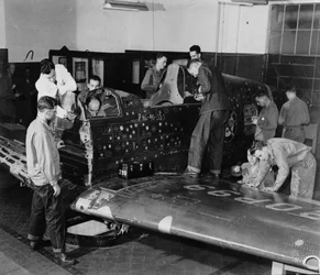 Soldier trainees work on “Flying Patch,” a Curtiss “Warhawk” fighter plane without engine or tail assembly, with simulated bullet holes and patches, c. 1942
