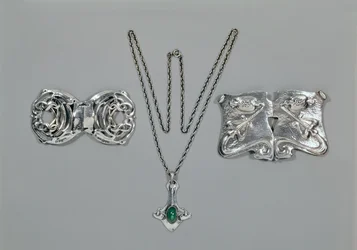 Silver jewellery designed for Liberty. Left to right: Waist clasp with interlaced Celtic design, 1904. Pendant and chain set with cabochon-cut chrysoprase. Waist clasp with repousse design on hammered