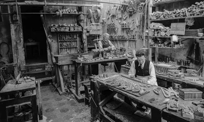 Artisans at a workbench in a workshop fabricating small wooden objects