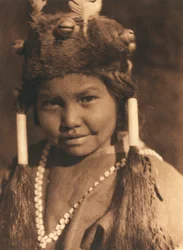 Close-up of an American Indian boy of the Klamath tribe or village. He is wearing a fur hat with applied acorns and feathers and wears his hair in two ponytails